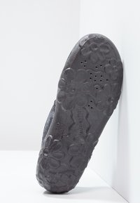 Svart gummiskosula med blommönster, texturerad yta och ventilationshål. Utformad för komfort och hållbarhet.