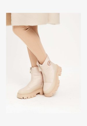 Beżowe, wodoodporne botki sięgające kostki z wyściełanym wierzchem, bocznymi zamkami błyskawicznymi i masywnymi gumowymi podeszwami z teksturowanym gripem. Okrąły logo na boku.