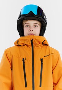 Oranje waterdichte skijas met zwarte accenten, ritszakken en ventilatiegaten. Zwarte skihelm met blauwe spiegelvizier.