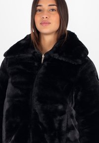 Giacca in finta pelliccia nera con ampio colletto, chiusura con zip e morbida consistenza pelosa. Progettata per calore e comfort.