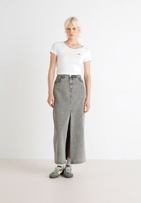 Weißes kurzärmeliges T-Shirt kombiniert mit einem langen, hellgrauen Jeansrock mit einem Schlitz vorne, getragen mit grünen Sneakers und weißen Socken.
