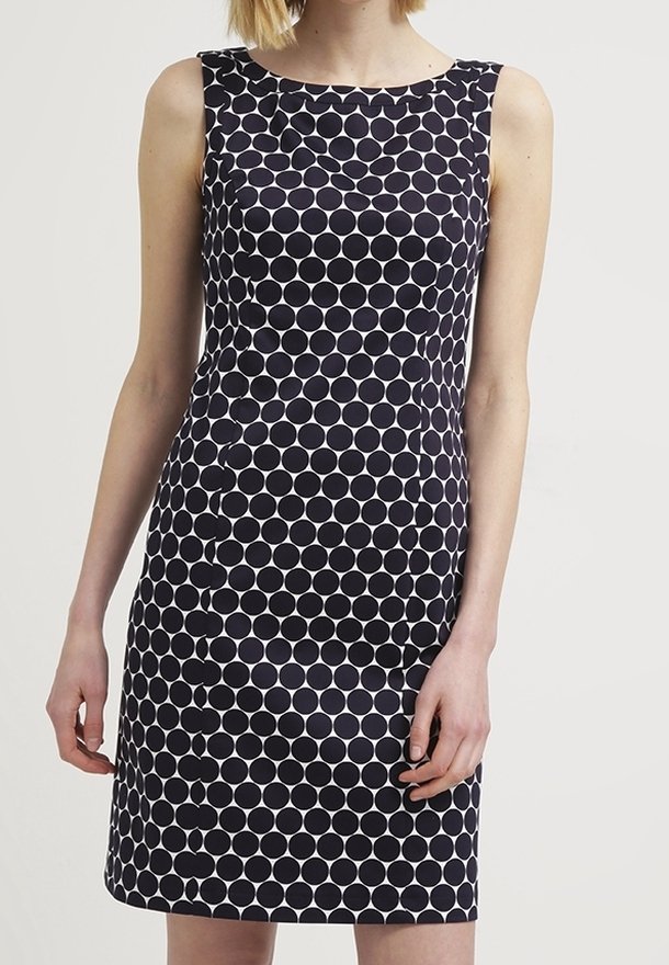 Robe ajustée sans manches avec un grand motif à pois noir et blanc, portée par une personne debout devant un fond uni clair.