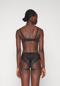 Svart spetslingerie-set med en bralette med justerbara band och hakstängning, i kombination med lågt skurna spetsunderbyxor.