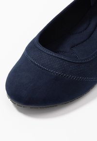 Chaussure plate en suede bleu marine avec une texture lisse, une tige perforée et un détail de couture contrastant le long de la couture. Semelle en caoutchouc flexible.