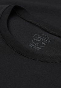 Primer plano del cuello de una camiseta negra de algodón con etiqueta impresa que muestra la marca, talla pequeña y detalles de fabricación.