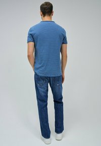 T-shirt à manches courtes bleu et blanc rayé, associé à un jean bleu foncé et des baskets blanches, vu de dos. Design simple, coupe décontractée.