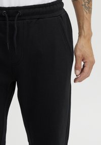 Pantalones de chándal de algodón negros con cintura elástica, cordón ajustable, bolsillos laterales y una textura suave y cepillada.