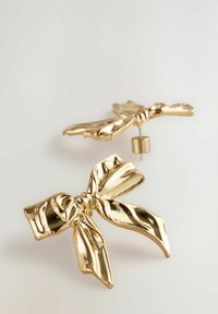 Ohrringe in Goldfarbe, die wie Schleifenbänder geformt sind, mit einer glänzenden Oberfläche und strukturierten Details in der Mitte und an den Rändern.