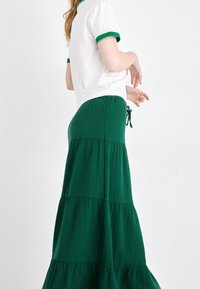 Valkoinen lyhythihainen paita, jossa on vihreä reunus, yhdistettynä pitkään, kerrokselliseen vihreään hameeseen, jossa on teksturoitu kangas ja kiristettävä vyötärönauha.