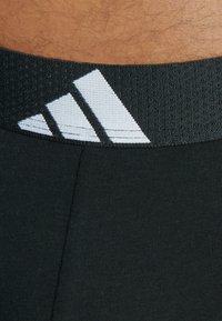 Svarta sporttights med en texturerad svart midja. Midjan har tre vita parallella ränder som logodetalj.