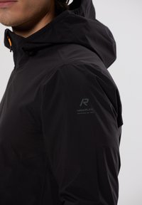 Sort vandtæt jakke med hætte, der har en glat tekstur og et reflekterende logo på ærmet. Lynlåsdetaljer i orange.