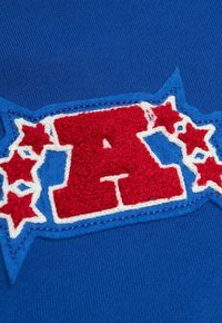 Tessuto blu con una "A" rossa ricamata circondata da una bordatura bianca e stelle rosse, caratterizzato da un design testurizzato su uno sfondo liscio.