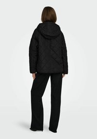 Czarna pikowana kurtka z kapturem, z motywem diamentu, widocznym przeszyciem i luźnym krojem. Połączona z luźnymi czarnymi spodniami.