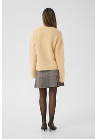 Hellgelbes, flauschiges Sweatshirt mit langen Ärmeln, kombiniert mit einem grauen karierten, plissierten Rock, dunklen Strumpfhosen und braunen hohen Schuhen.