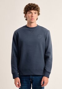 Sudadera marinera con cuello redondo, tejido ligeramente texturizado, puños y bajo acanalados, que presenta un sutil logo en relieve en el pecho.