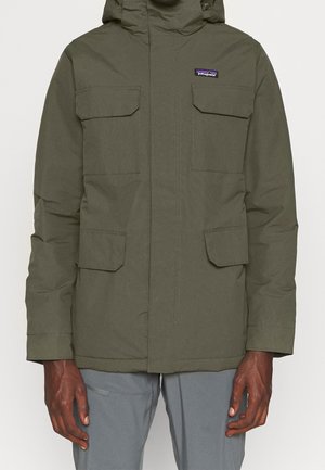 Hombre con chaqueta Patagonia verde oliva con cuatro bolsillos frontales con solapa y capucha, combinado con pantalones grises.