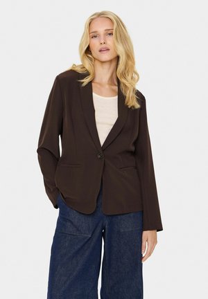 Dark brown blazer with a single button, two front pockets, and long sleeves, paired with a light top and blue wide-leg pants.