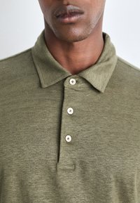 Olivgrön polo-tröja i mjukt tyg, med vikbar krage, tre-knapp placket och subtil textur.