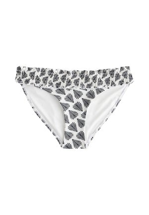 Kobieta ubrana w biały bikini z niebieskimi wzorami liści, stojąca na jasnym tle z miękkimi cieniami.