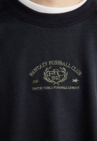 Czarna bluza z prążkowanym kołnierzem, wyszywanym zielonym logo "Fantazy Fussball Club" oraz napisem "United Table Fussball League".