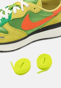 Grön och gul mocka- och tygsneaker med orange detaljer och vita skosnören; inkluderar två neon gula skosnören.