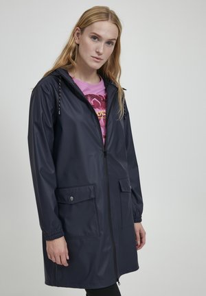 Marineblaue Regenjacke mit Frontreißverschluss, zwei Seitentaschen, elastischen Bündchen und verstellbarem Kapuzenbereich. Hergestellt aus wasserdichtem Material.