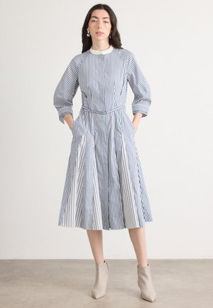 Gestreepte jurk in wit en marineblauw, met een ronde halslijn, gathered taille, lange mouwen en zijzakken, gecombineerd met beige enkellaarsjes.