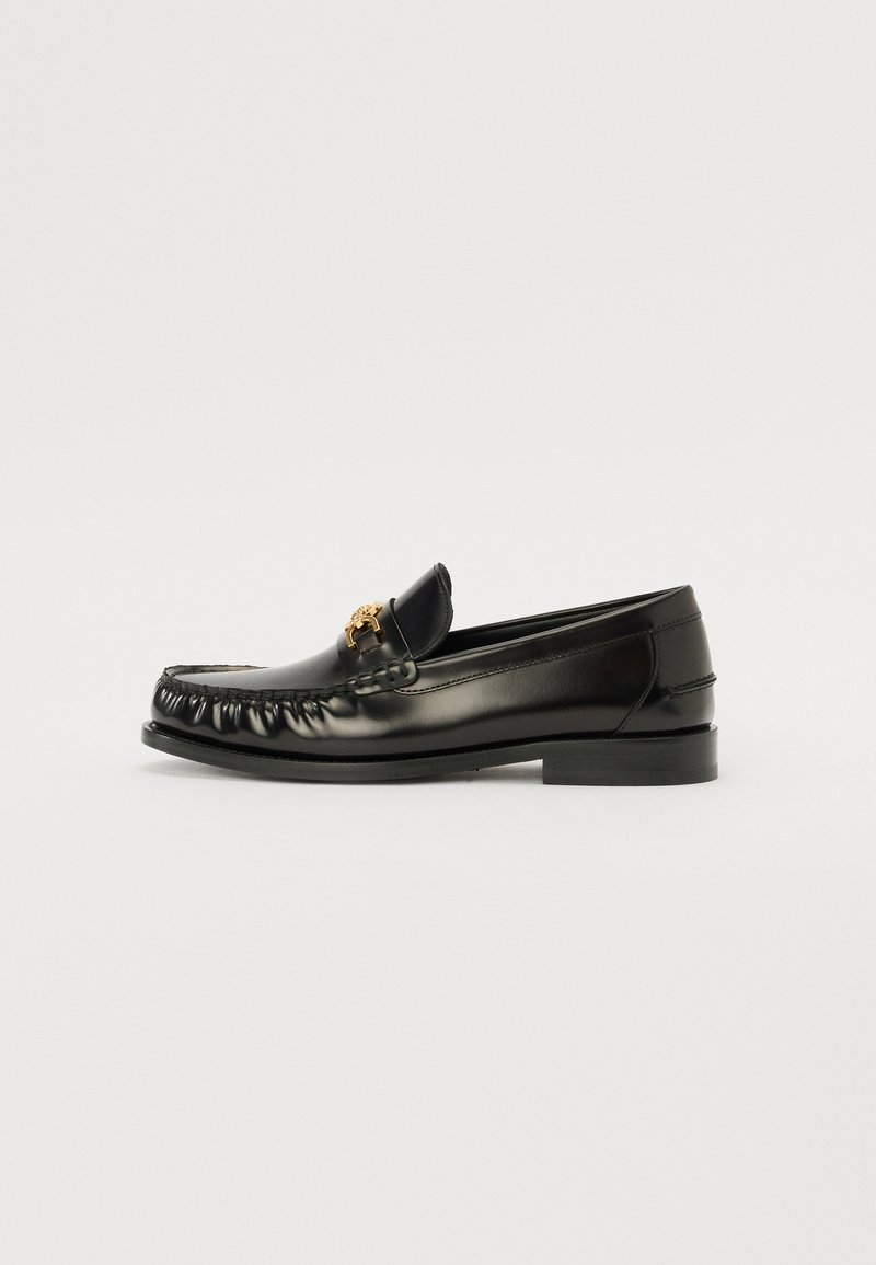Svarta läderloafers med rund tå, med en guld dekoration på ovandelen och subtila stygn längs kanterna. Platt sula.