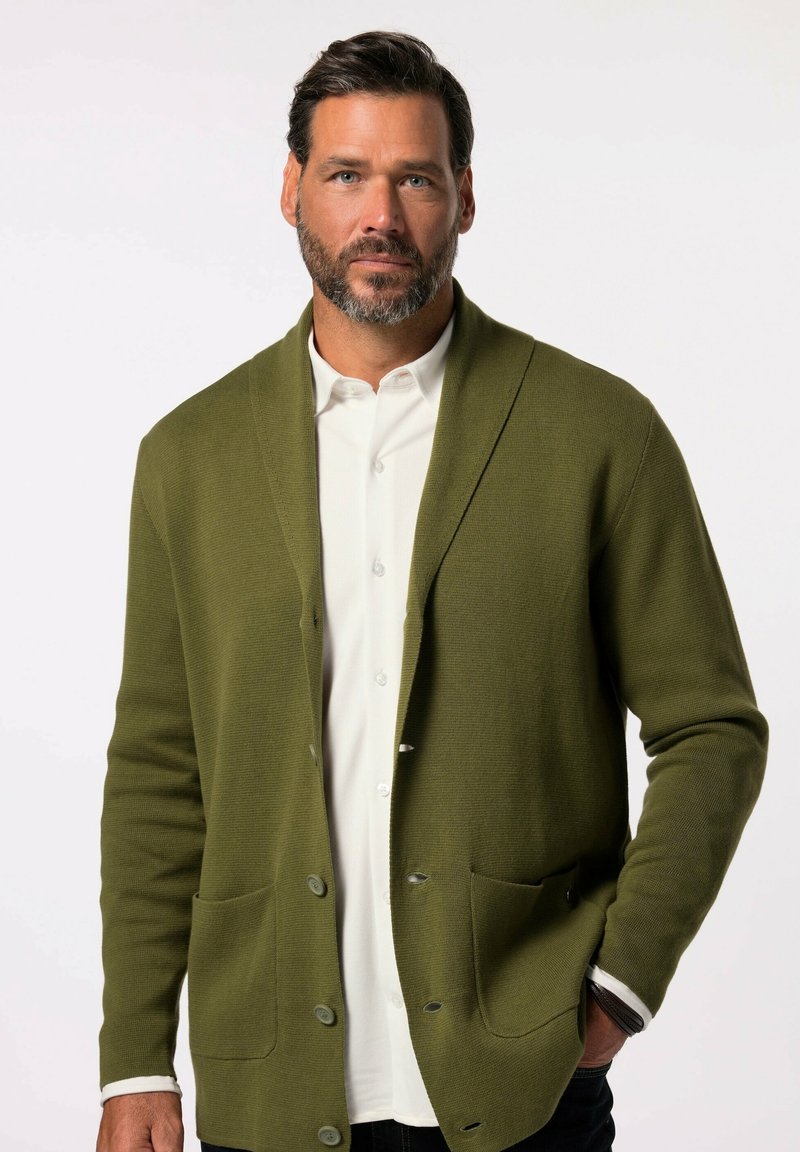 Olivgrüner Strickcardigan mit einem Schalkragen, zwei Fronttaschen und Knöpfen aus einem strukturierten Stoff. Über einem weißen Hemd getragen.