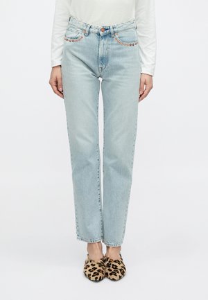 Šviesiai mėlynos aukšto liemens džinsinės kelnės su tiesiomis kojomis, dekoruotos metaliniais smeigtukais palei juosmenį. Derinamos su leopardo rašto butais.