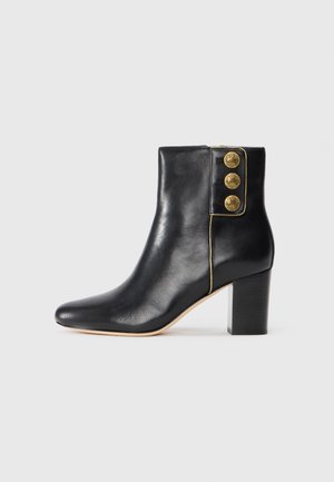 Botte de cheville en cuir noir avec un bout pointu et un large talon. Présente trois accents en boutons dorés sur le côté et un profil élancé.
