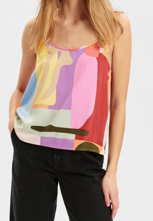 Femme portant un haut sans manches avec des formes abstraites colorées en tons pastel et vifs, assorti à un pantalon noir.