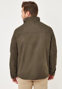 Olivgrüne Jacke mit Kragen, strukturiertem Stoff und geknöpften Ärmeln. Verfügt über ein gesteppter Rückenpanel und ein dezentes Logodetail.