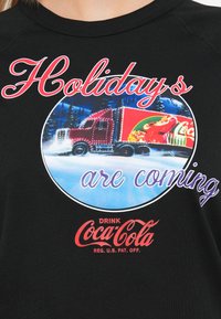Świąteczny ciężarówka Coca-Cola jadąca przez zaśnieżony las z napisem "Święta się zbliżają" na czarnym tle.
