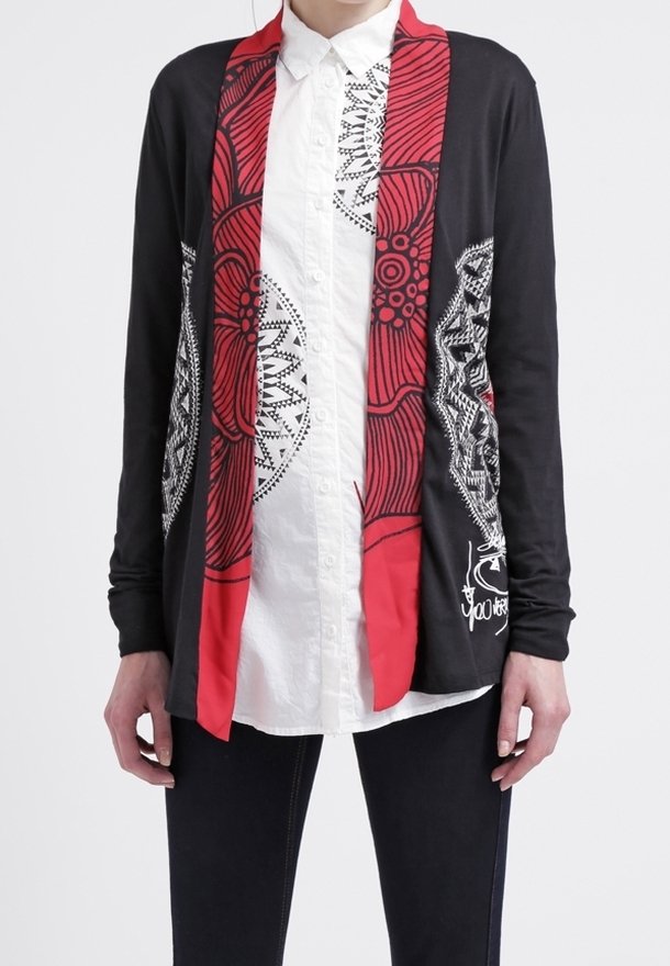 Personne portant un cardigan noir avec des motifs abstraits rouges et blancs sur une chemise blanche boutonnée et un pantalon noir.