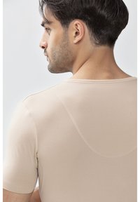 Camicia beige a maniche corte con scollatura tonda, texture liscia e dettagli di cucitura discreti lungo le cuciture.