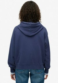 Sudadera azul marino con capucha, presenta un corte relajado y puños acanalados. Combinada con jeans de mezclilla de un azul claro, exhibiendo un estilo casual.