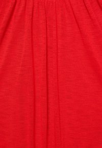 Tissu rouge avec une texture fine tricotée et des plis froncés créant des plis verticaux.