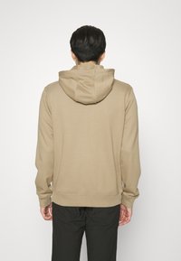 Beige Kapuzenpullover aus Stoff, mit entspannter Passform, gerippten Bündchen und Saum. Glatte Textur mit minimalistischem Design, ohne sichtbare Muster.