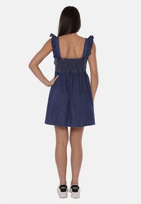 Abito in denim con spalline arricciate, corpetto smock e gonna a campana. Colore blu scuro, di lunghezza media, con vita arricciata e superficie liscia.