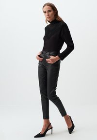 Maglione nero a coste con yoke testurizzato, abbinato a pantaloni aderenti in ecopelle nera e décolleté slingback nere con punta affilata.