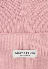 Roze gebreide muts met een textuurpatroon. Voorzien van een wit label met de tekst "Marc O’Polo EST. IN STOCKHOLM." Het materiaal oogt zacht en warm.