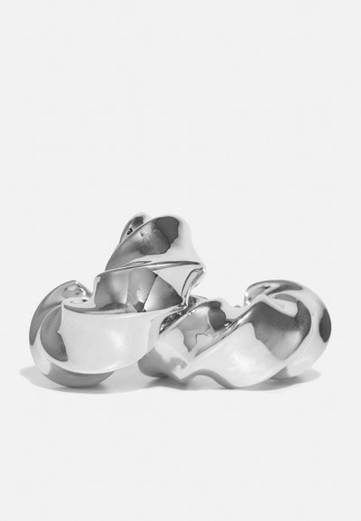 Sculptură din metal argintiu răsucit, cu o suprafață netedă și reflectorizantă. Prezintă forme curbate și o combinație de margini rotunjite și ascuțite.