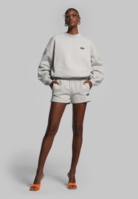 Grijze sweatshirt en short set, zachte textuur, losse snit. Sweatshirt heeft een dropped shoulder, shorts hebben een elastische tailleband en logo-detail.