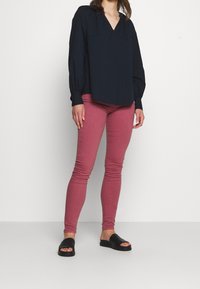 Mörkblå blus med v-ringning, långa puffärmar, tillsammans med rosa smala jeans och svarta slid-on sandaler. Slät, lätt vikt tyg.