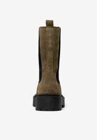 Botas de tobillo de ante caqui con un panel lateral elástico negro, superficie texturizada y una suela gruesa de goma negra. Cuenta con una lengüeta en la parte posterior.