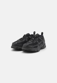 Chaussures de sport noires avec une tige en mesh, une semelle en caoutchouc épaisse, des accents texturés et une languette pour un enfilage facile.
