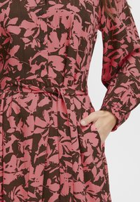 Rochie florală cu un model roz și maroniu, față cu nasturi, talie cu brâu, fustă pliată și mâneci lungi cu manșete elastice.