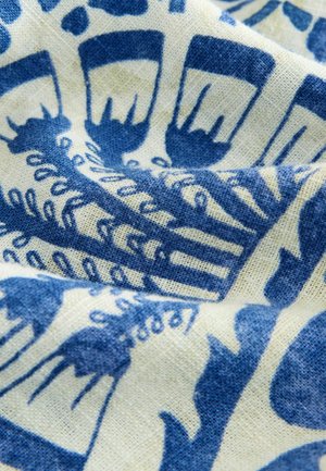 Modrý a bílý vzorovaný textil, který obsahuje složité květinové a abstraktní vzory, s texturovaným, tkaným vzhledem.