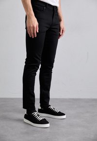 Svarta slim-fit jeans med fem fickor och subtila sömnadsdetaljer, i kombination med svarta mockaskor med vita gummisulor och snörning.